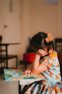 A young girl engrossed in reading a book in an indoor classroom setting.